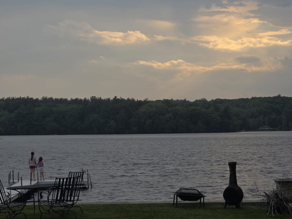 Two girls standing on a dock overlooking a lake at sunset