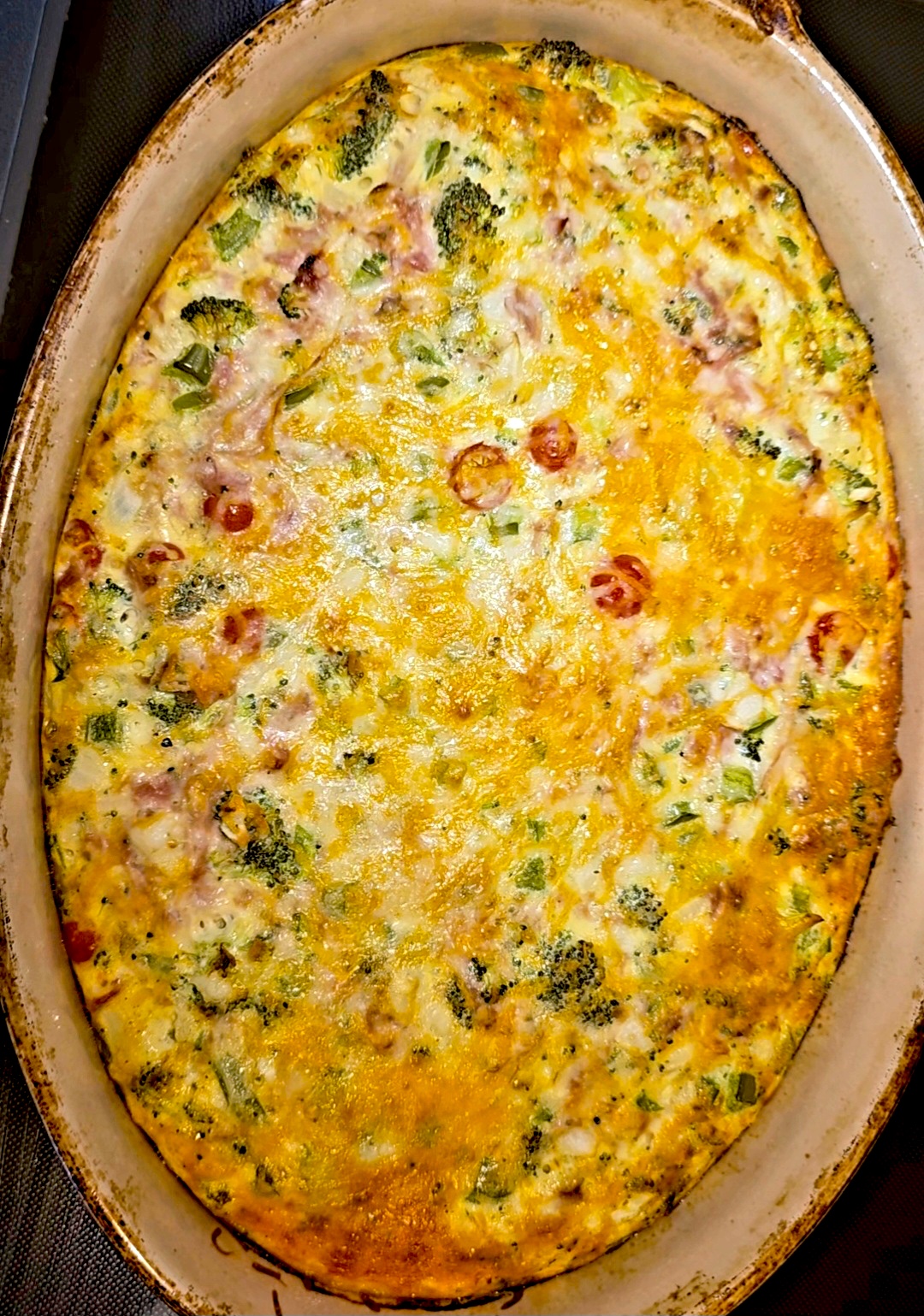 Breakfast egg bake with broccoli, ham, cherry tomatoes, and melted Colby Jack in an oval baking dish